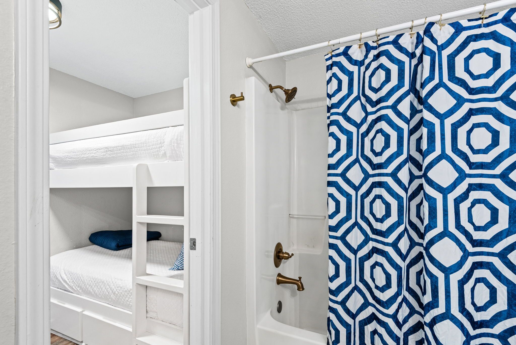 A white room with a bunk bed, a shower, and a patterned curtain.