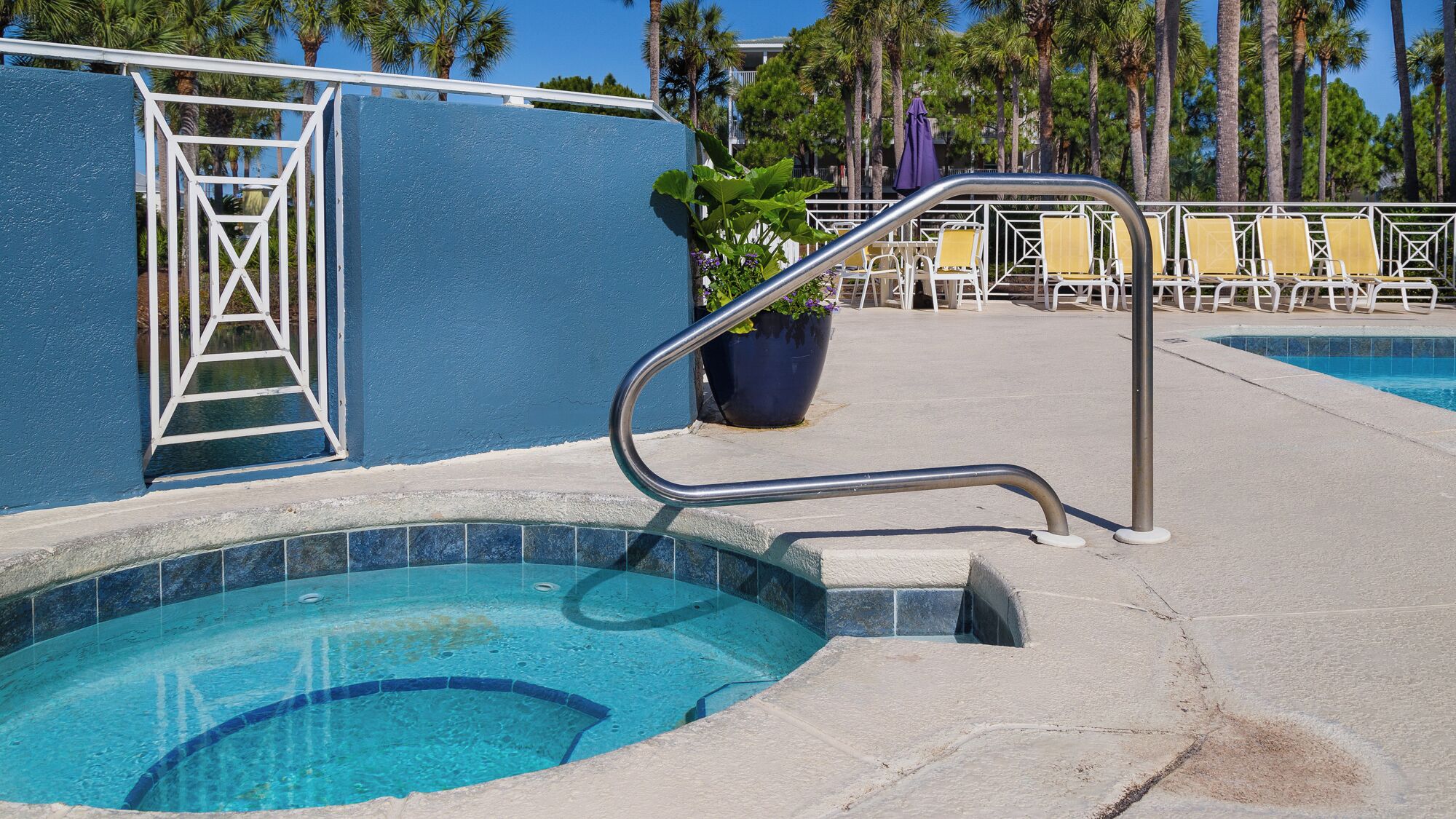 A pool area with a blue wall, a metal ladder, and lounge chairs.