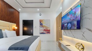 A modern hotel room with a large bed, a flat-screen TV mounted on the wall, a wooden headboard, and a marble floor.