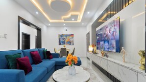 A modern living room with a blue sofa, a white coffee table, and a large TV on the wall.