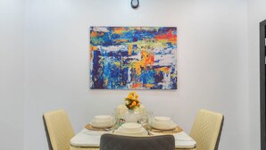A dining area with a table set for four, featuring a colorful abstract painting above and a vase with flowers on the table.