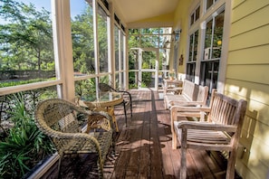 Een houten terras met rieten stoelen en een tafel, met uitzicht op een tuin met bomen en planten.