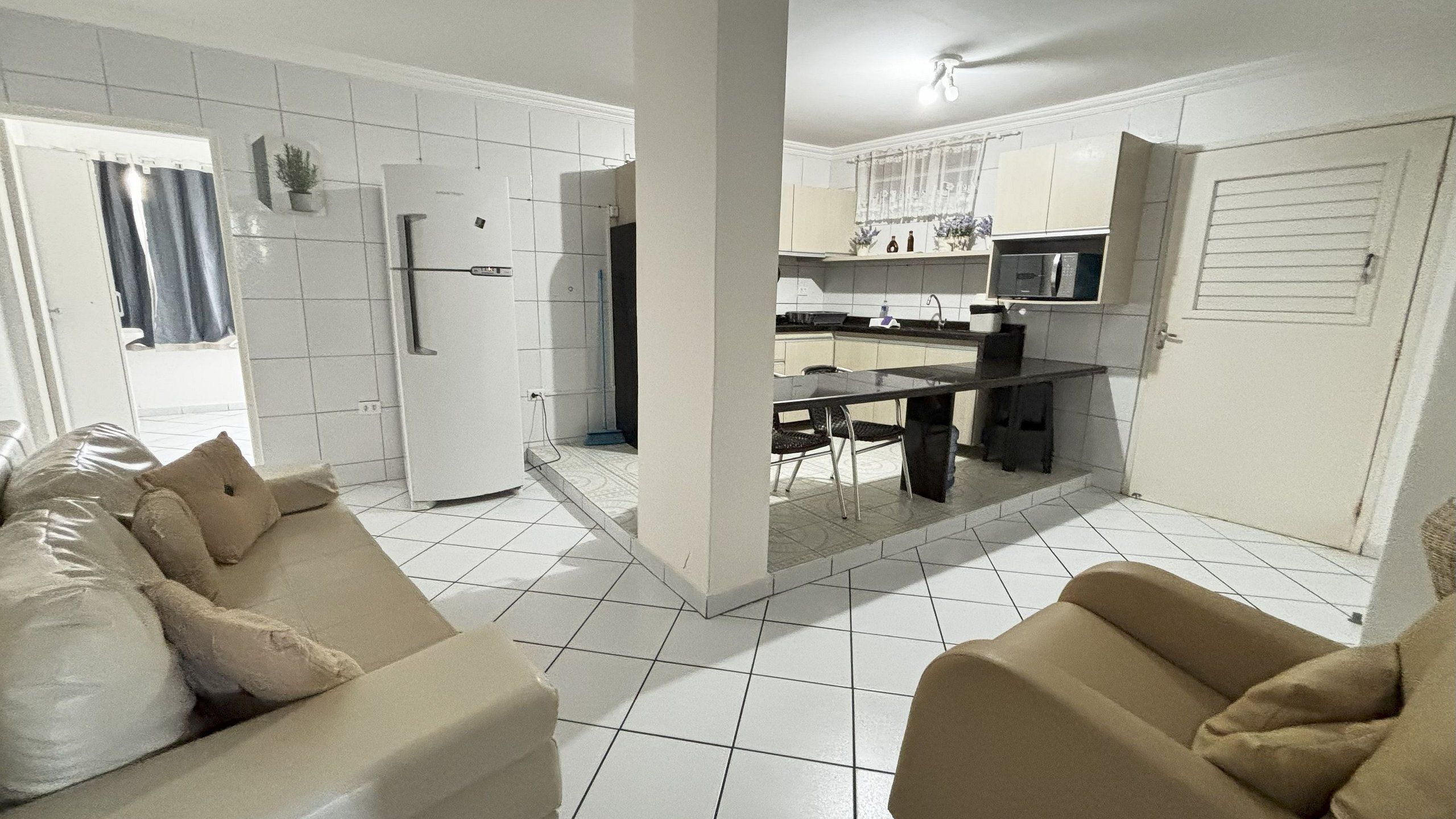 Una cocina moderna con armarios blancos, un comedor con mesa y sillas, y una sala de estar con sofá.