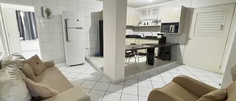 Una cocina moderna con armarios blancos, un comedor con mesa y sillas, y una sala de estar con sofá.