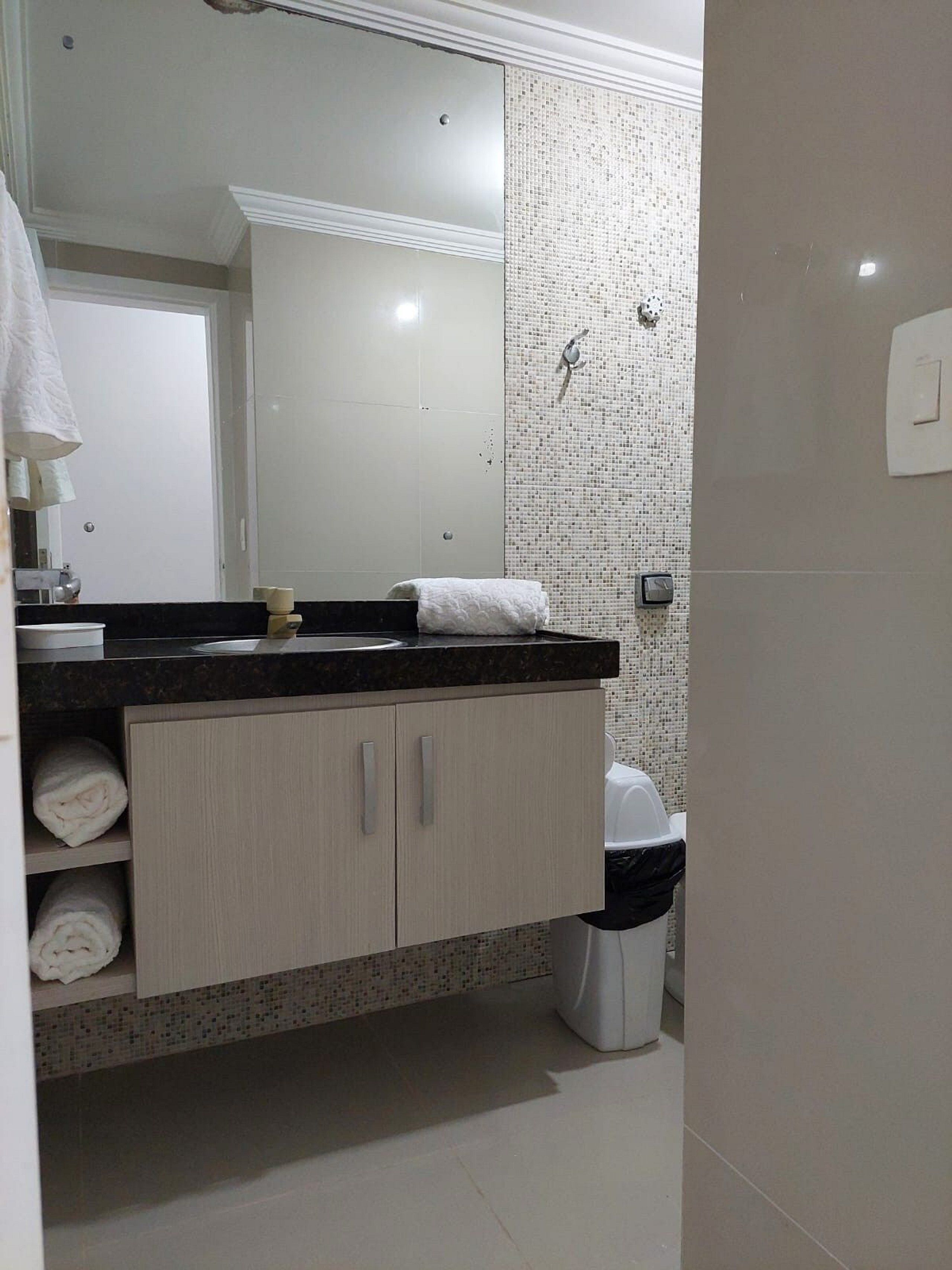 A bathroom with a mirror, sink, towel rack, and a trash bin.