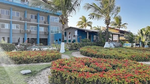Un hotel de varios pisos, con mesas al aire libre y un jardín bien cuidado con flores rojas.