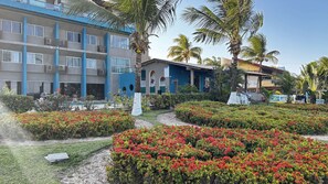 A hotel with multiple floors, outdoor seating, and a well-maintained garden with red flowers. - Marinas Tamandaré próximo à Carneiros  (Tamandaré)