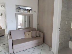 Un sofá color beige con cojines, un espejo encima y suelo de baldosas.