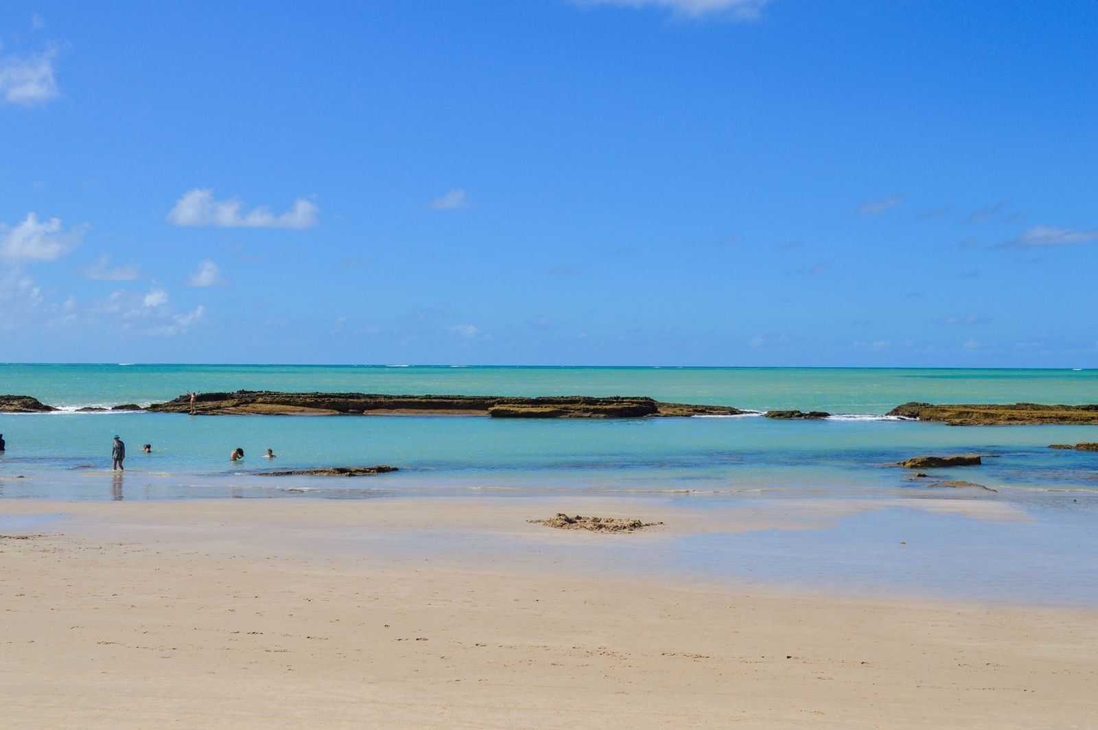 A beach with clear turquoise water, rocky outcrops, and a sandy shore.