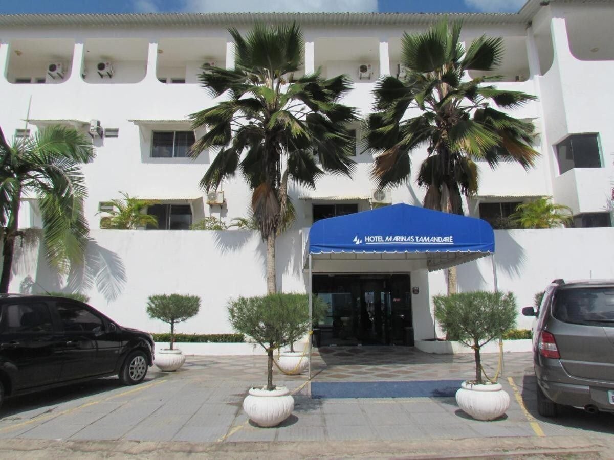 A hotel entrance with a blue awning, palm trees, and a parking lot.