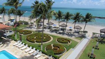 A resort with a pool, sun loungers, palm trees, and a beach view.