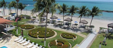 A resort with a pool, sun loungers, palm trees, and a beach view.