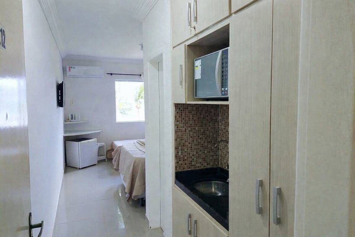 A compact hotel room with a kitchenette, a bed, and a window providing natural light.