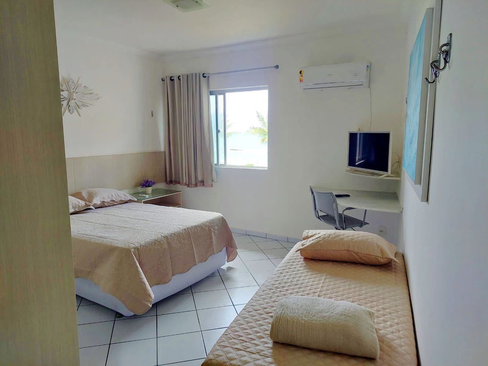 Habitación de hotel con dos camas, un escritorio con silla, televisor y aire acondicionado.