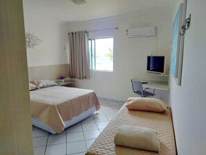 Habitación de hotel con dos camas, un escritorio con silla, televisor y aire acondicionado.
