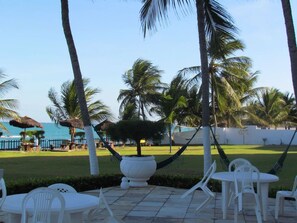 Un patio con sillas y mesas de plástico blanco, palmeras y vista al océano.
