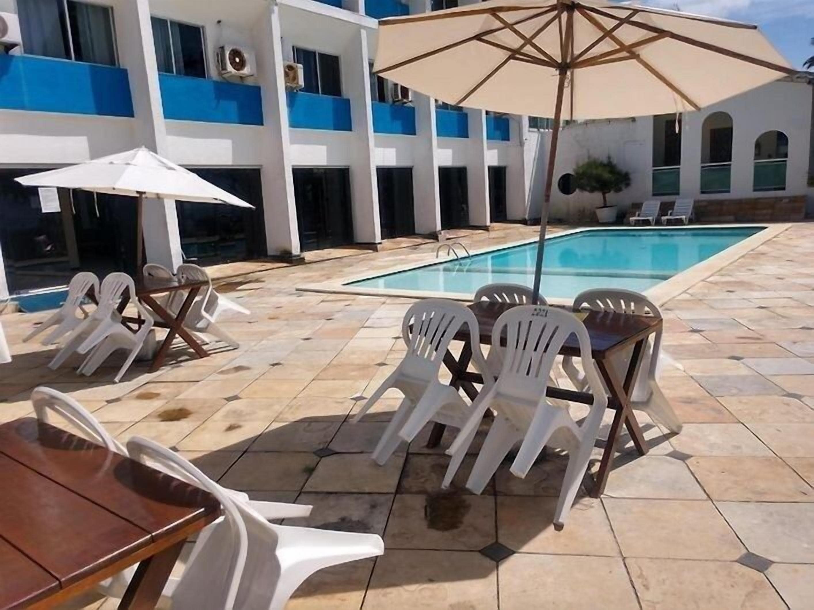 Un área junto a la piscina con sillas de descanso, una mesa y sombrillas.