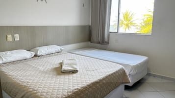 A hotel room with a large bed, a smaller bed, a window with a view of palm trees, and a curtain.