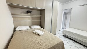 A bedroom with a bed, a bedside table, a small potted plant, and a door leading to another room. - Marinas Tamandaré próximo à Carneiros  (Tamandaré)