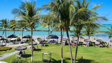 A resort with a beach view, palm trees, and thatched umbrellas.