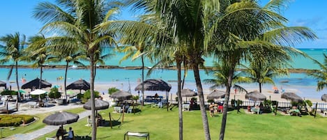 Un complexe hôtelier avec vue sur la plage, des palmiers et des parasols en feuilles de palmier.