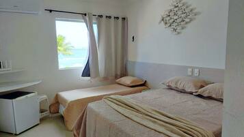 A hotel room with two beds, a window with curtains, a wall-mounted light fixture, and a small white appliance.