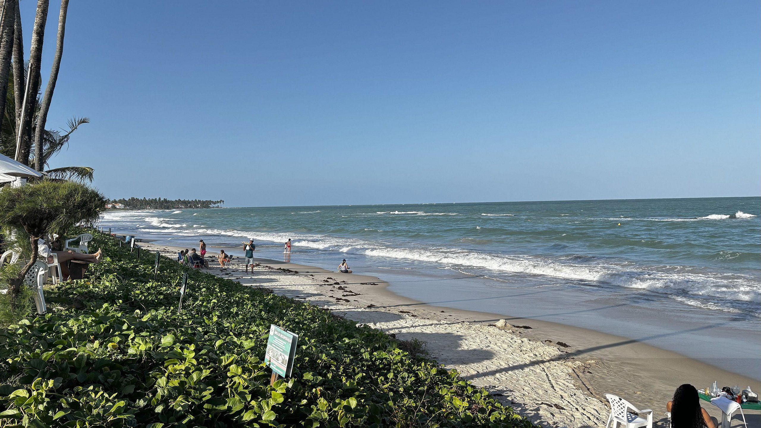 A beach with people, a sign, and a view of the ocean.