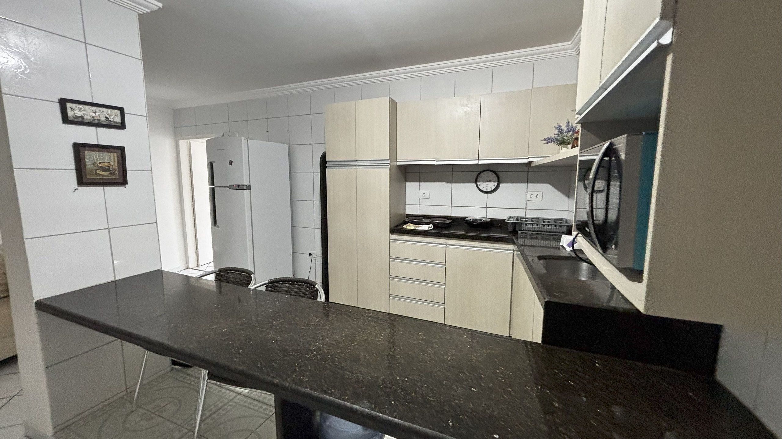 A kitchen with white cabinets, a black countertop, a microwave, and a clock on the wall.