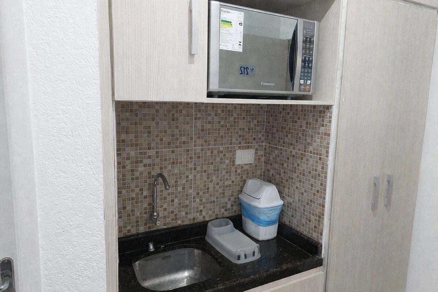 A compact kitchenette with a microwave, sink, and tiled backsplash.
