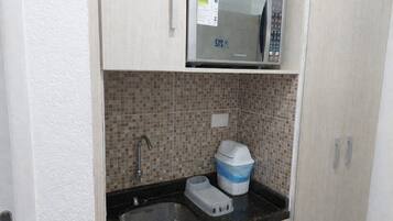 A compact kitchenette with a microwave, sink, and tiled backsplash.