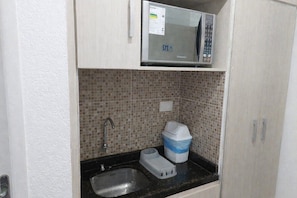 Una kitchenette compacta con microondas, pileta y salpicadero de cerámica.