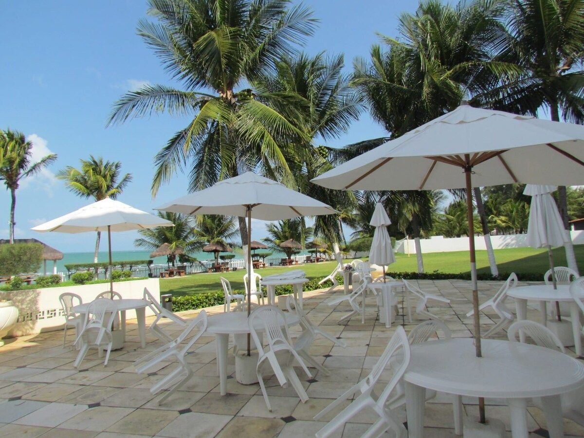 Outdoor seating with umbrellas, palm trees, and a view of the ocean.