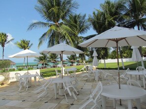 Outdoor seating with umbrellas, palm trees, and a view of the ocean. - Marinas Tamandaré próximo à Carneiros  (Tamandaré)