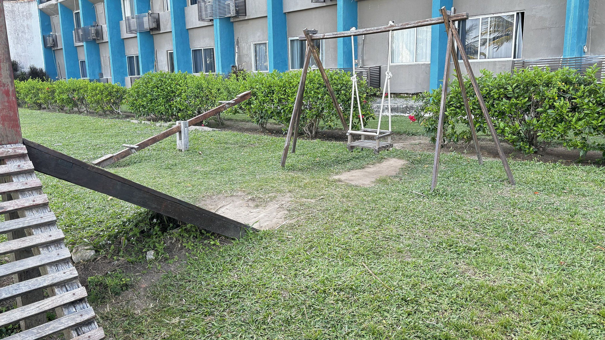A grassy area with a wooden swing set and a concrete path.