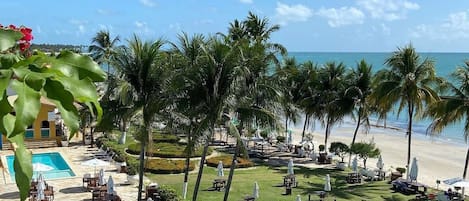 A resort with a pool, outdoor seating, palm trees, and a beach view.