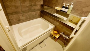 Une salle de bain moderne avec une grande baignoire, un petit tabouret en bois et une étagère contenant des articles de toilette.