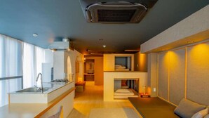 A compact hotel room with a kitchenette, a sofa, and a small dining area.