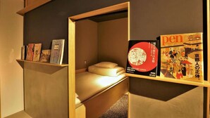 A compact room with a bed, a shelf with books, and a wall-mounted book titled "Art History 1945-2014: Japan".