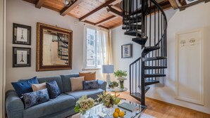 Un salon avec un canapé bleu, une table basse en verre et un escalier en colimaçon noir.