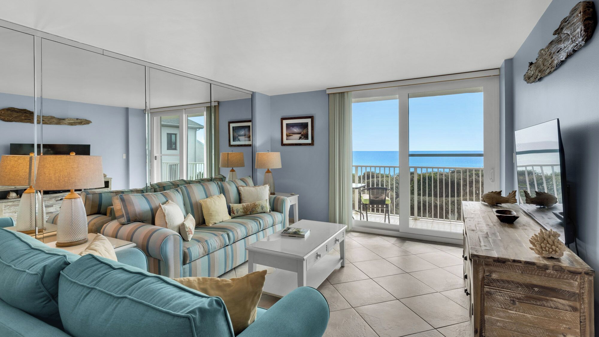 A modern living room with a large sofa, a coffee table, and a view of the sea through a balcony.