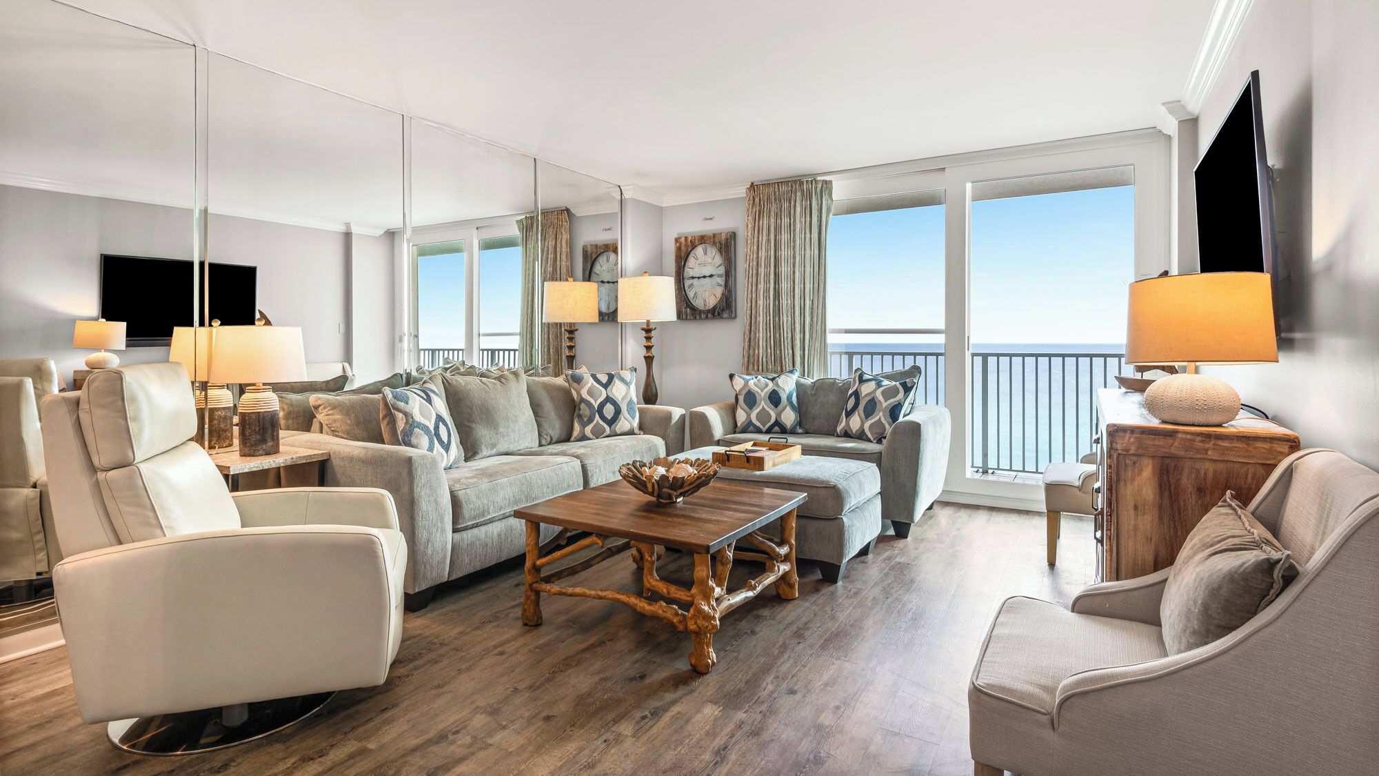 A spacious living room with a large sofa set, a wooden coffee table, and a view of the sea through large windows.