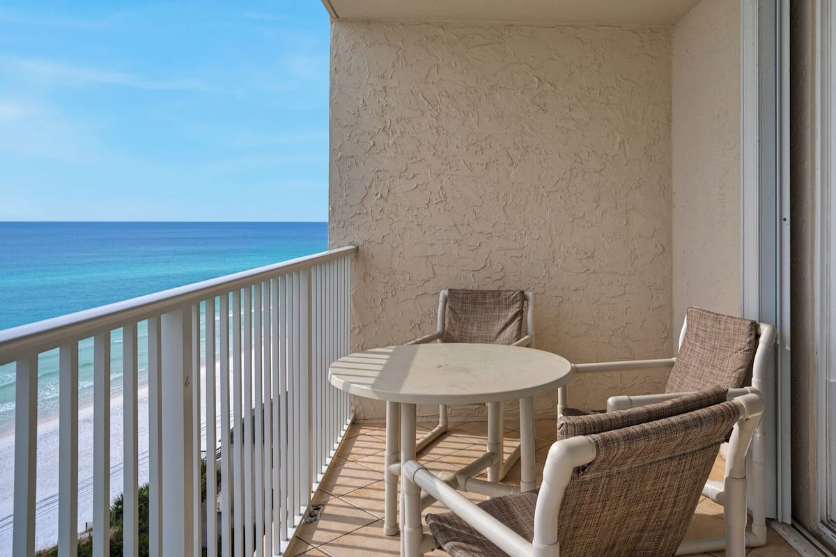 A balcony with a white railing, a round table, and two wicker chairs.