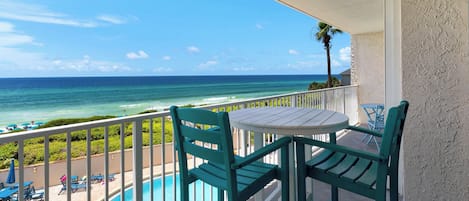 A balcony with a view of the ocean, a pool, and outdoor seating.