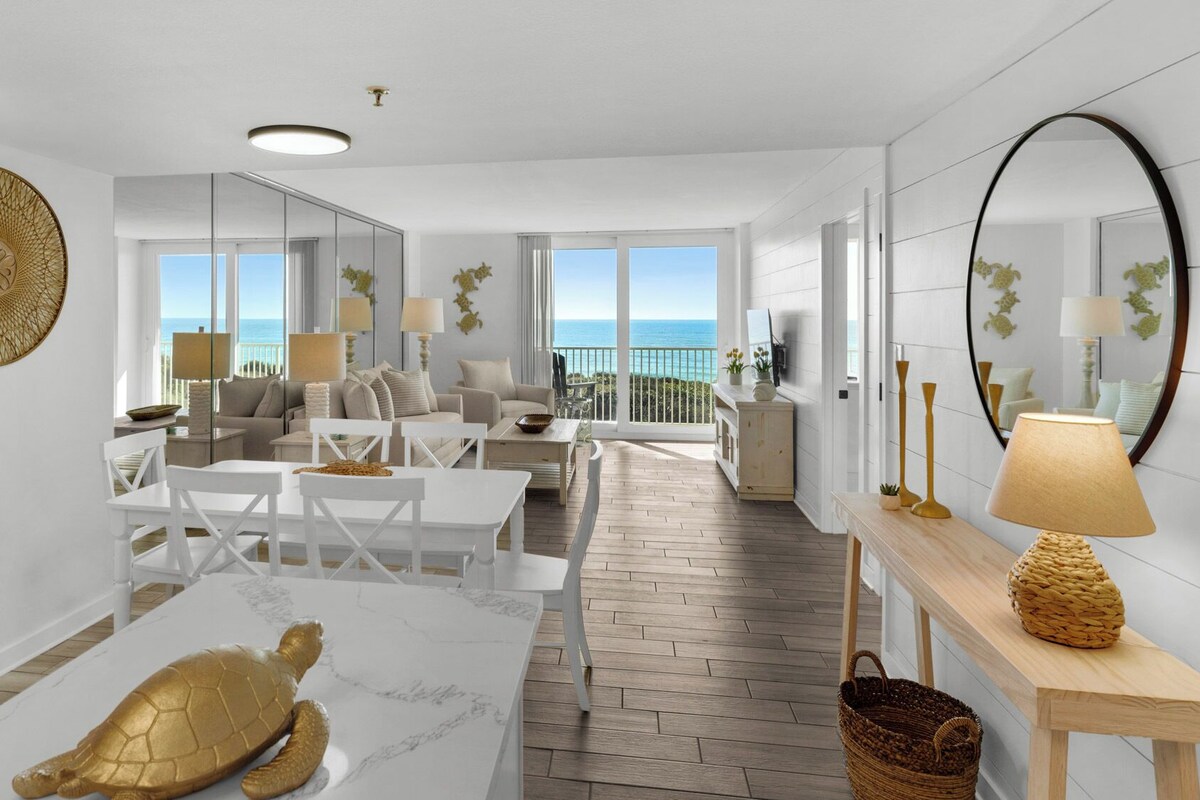 Amplia sala de estar con vista al océano, una mesa de comedor con una escultura de tortuga y un balcón con vistas.