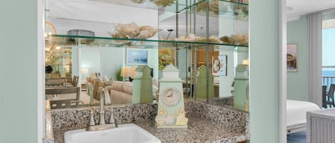 A bathroom with a granite countertop, a white sink, and a decorative clock.