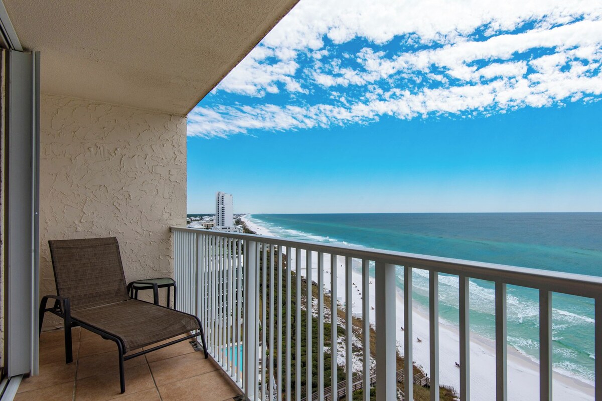 Un balcón con vista al océano y a la playa, una silla y una barandilla.