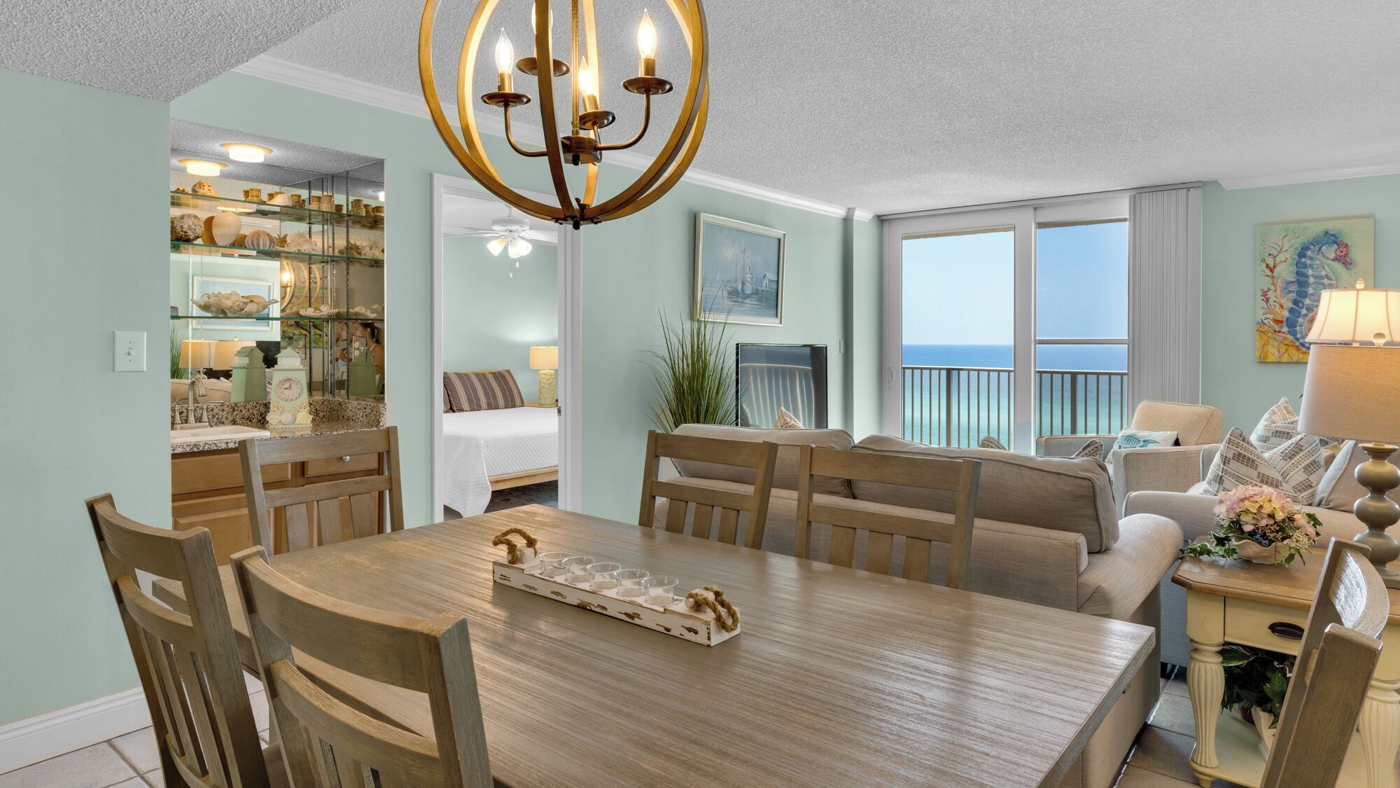 A spacious dining area with a wooden table and chairs, a chandelier, and a view of the ocean through large windows.