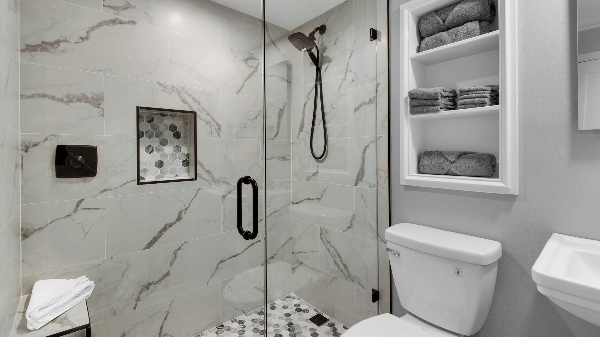 A modern bathroom with a glass-enclosed shower, a toilet, and a shelf with towels.