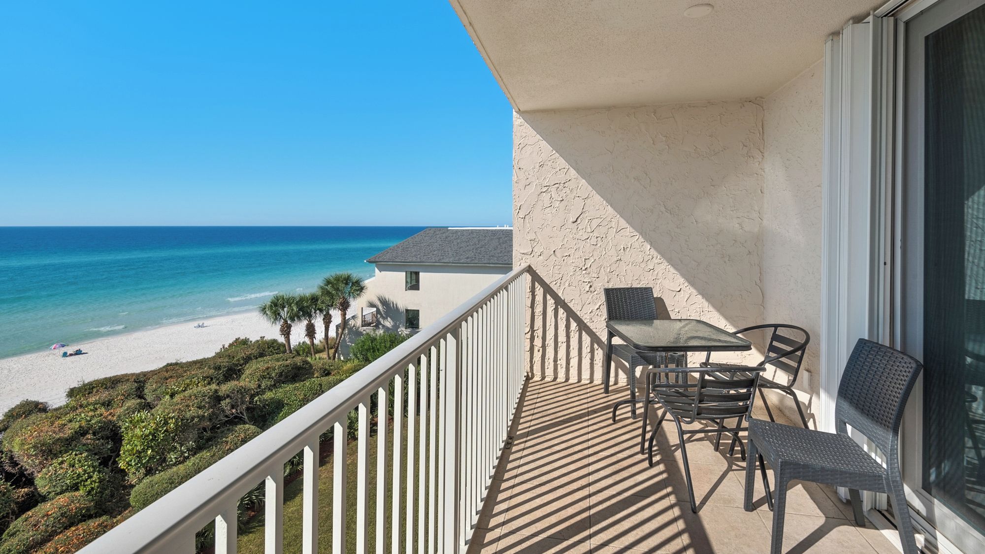 A balcony with a table and chairs overlooking a beach and ocean.