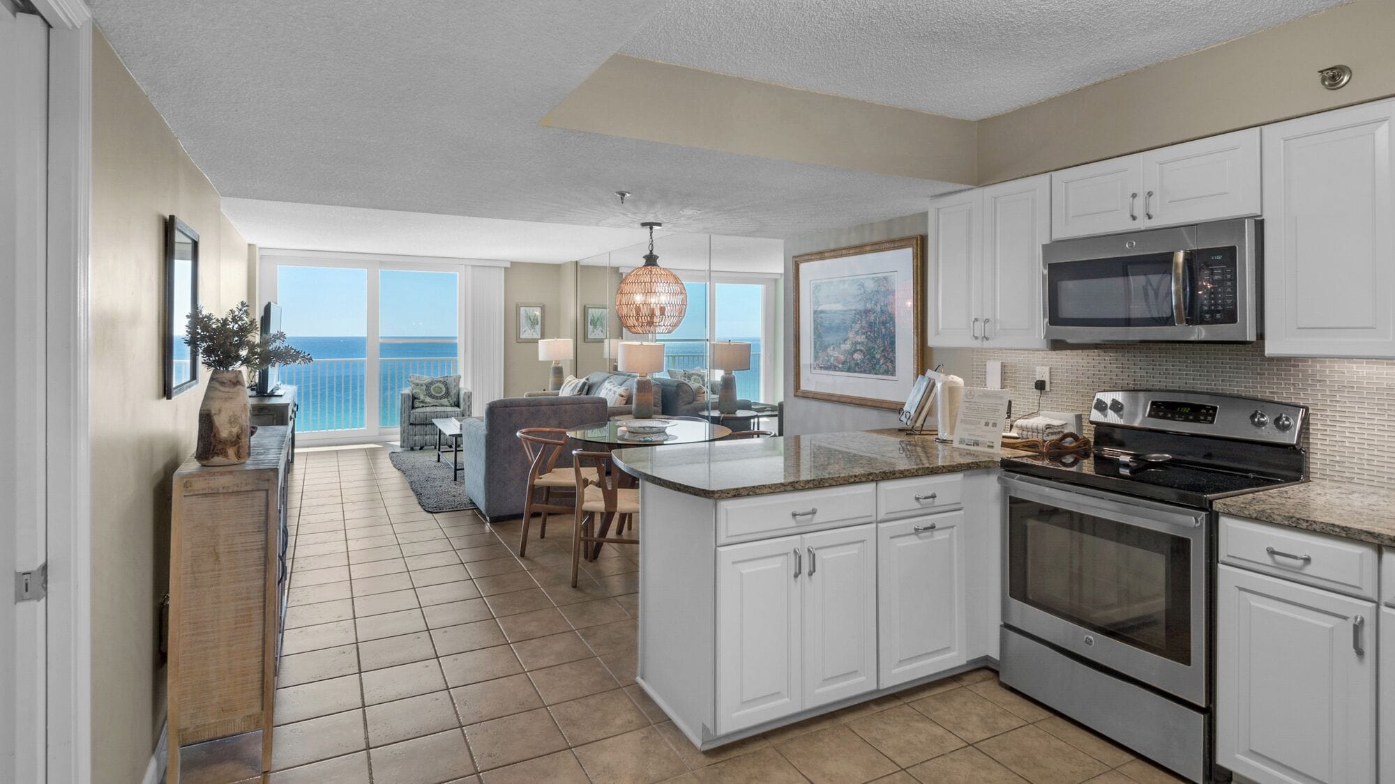 A spacious kitchen with white cabinets, a granite countertop, and stainless steel appliances. There is a dining area with a view of the ocean.